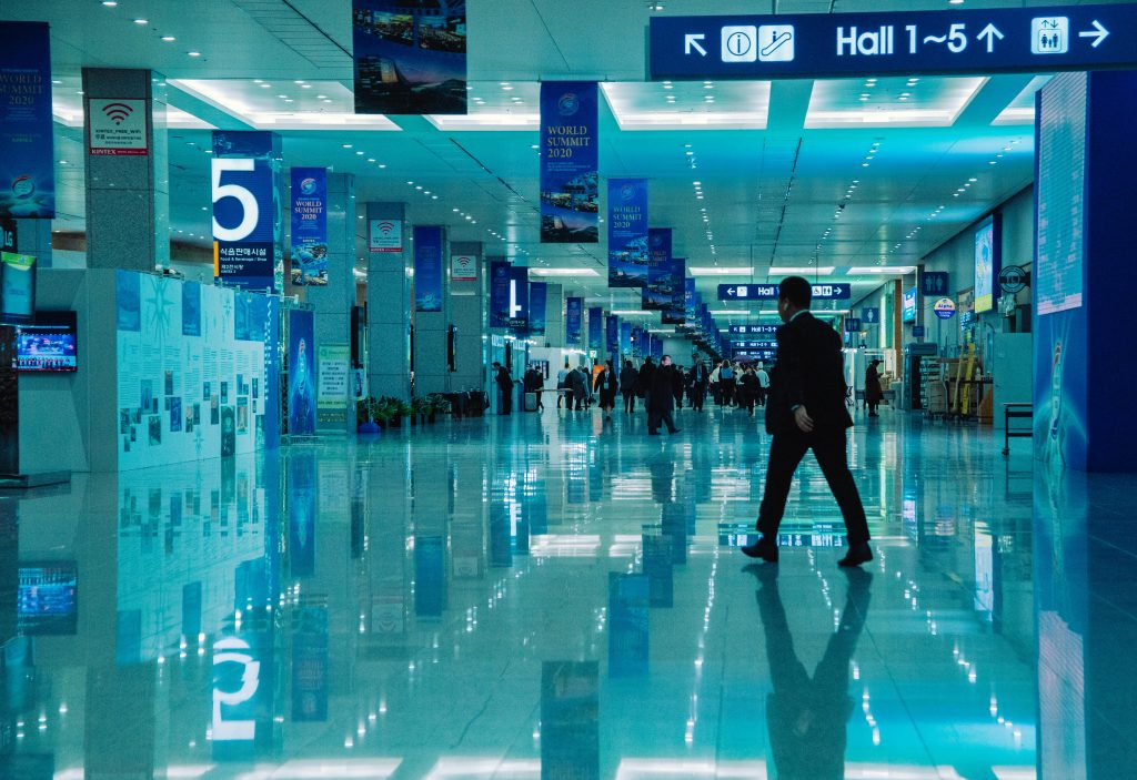 An indoor view of a busy conference hall during World Summit 2020 with directional signs and reflections.