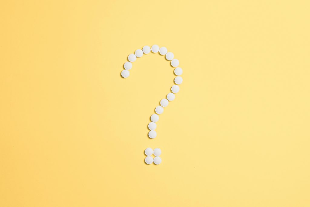 White pills arranged into a question mark shape on a vibrant yellow background.